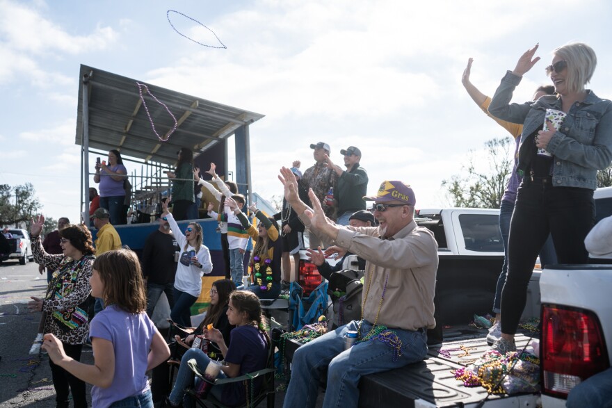 A crowd cheers as beads fly through the air at a children's parade.