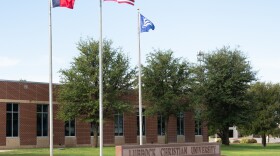 A photo of a Lubbock Christian University sign with the Texas flag, U.S. flag, and LCU flag above it.