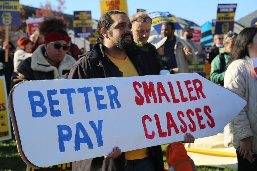 Man holds a large sign that reads "Better pay smaller classes".