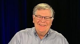 A man with a grey shirt and glasses smiles at the camera.