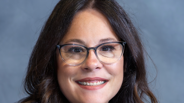 A portrait-style photo of a woman with shoulder-length brown hair. She is wearing glasses and a blue zip-up. 