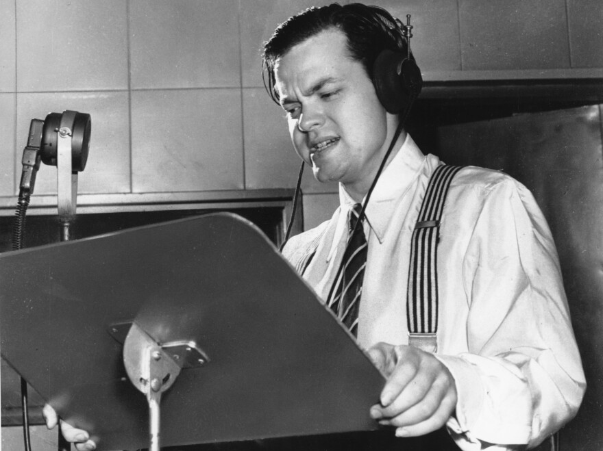 Orson Welles delivering a radio broadcast in 1938, the same year he aired his <em>War of the Worlds</em> fake news program.