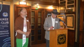 Milwaukee musician Paul Cebar stands next to a podium while a member of the Milwaukee Press Club addresses the audience.