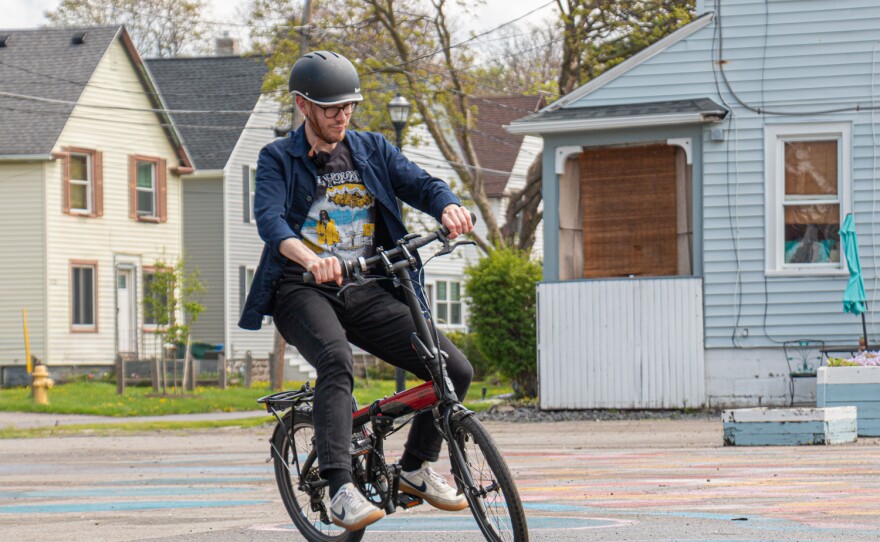 A man wearing a helmet rides his bicyle by a blue house.