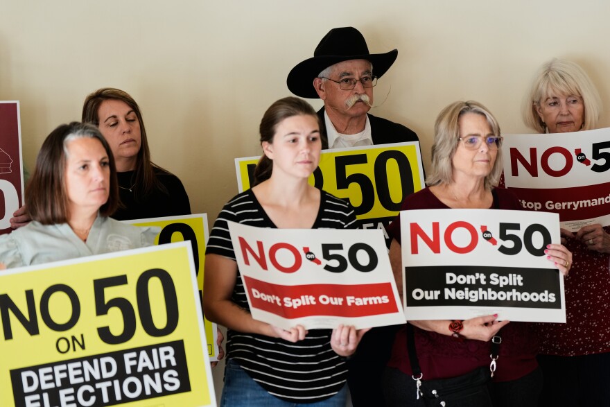 People hold up signs opposing Prop 50 during a press conference in Chico, Calif., Wednesday, Oct. 29, 2025.