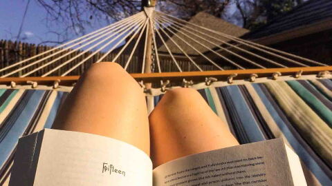 color photo of person reading a book on a hammock