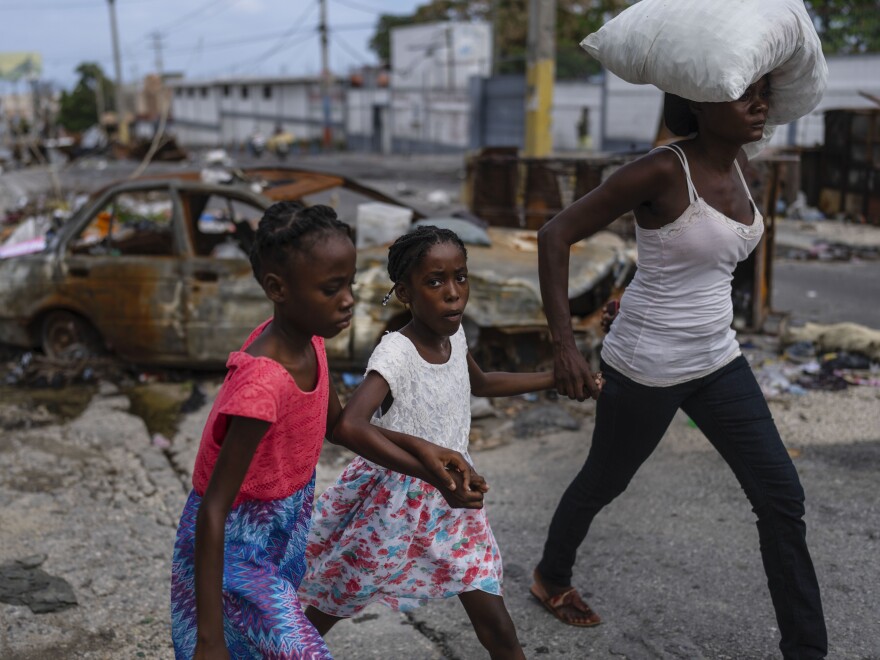 Girls holding hands are led past a burnt car blocking the street as they evacuate the Delmas 22 neighborhood to escape gang violence in Port-au-Prince, Haiti, May 2, 2024.