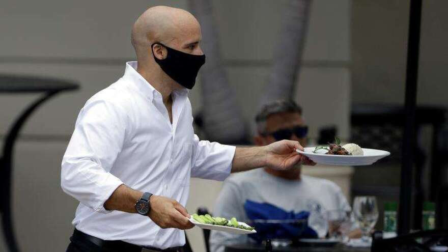 A food server wears a protective face mask as he delivers food to customers at the Parkshore Grill restaurant Monday, May 4, 2020, in St. Petersburg, Fla. Several restaurants are reopening with a 25% capacity as part of Florida Gov. Ron DeSantis' plan to stop the spread of the coronavirus. (AP Photo/Chris O'Meara)