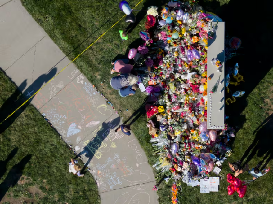 An aerial view of a memorial of flowers, balloons, and sidewalk chalk near a grassy area.