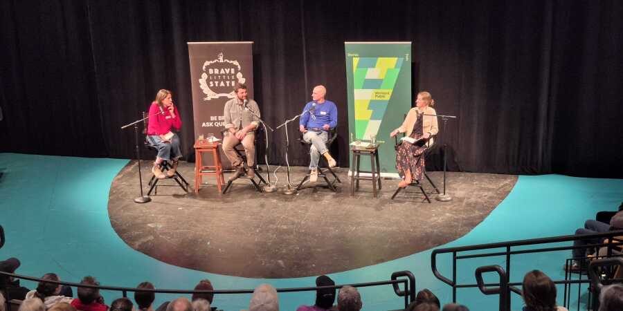 four people sit on chairs facing a seated audience