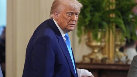 A man stands in a suit holding a jersey. 