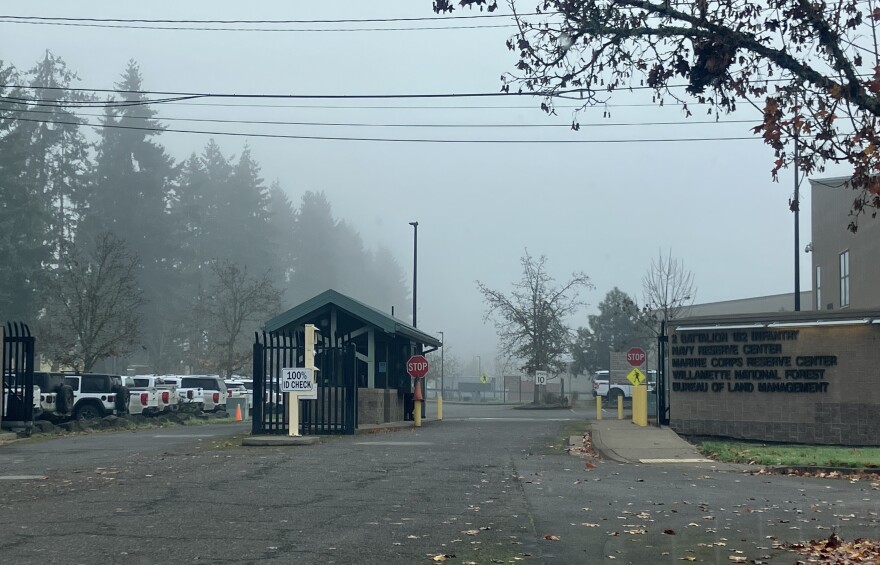 An entrance to a government facility. There is a guard house and a stop sign. 