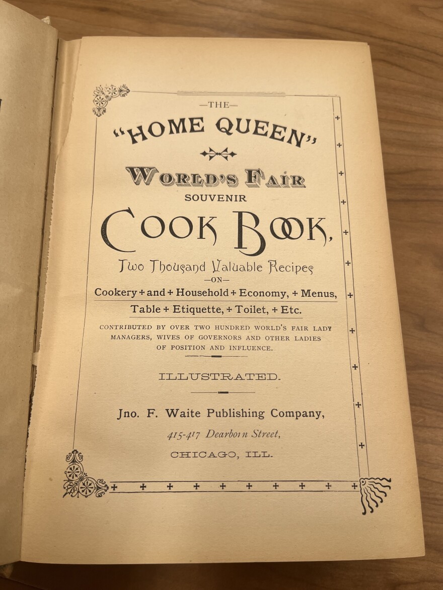 A book is open to the title page, which reads, "The 'Home Queen' World's Fair Souvenir Cook Book. Two Thousand Valuable Recipes."