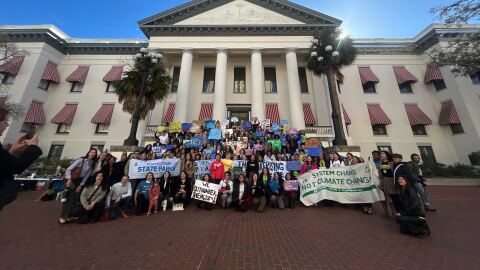 A group of young environmental activists holding signs stand in front of the Old Capitol Building