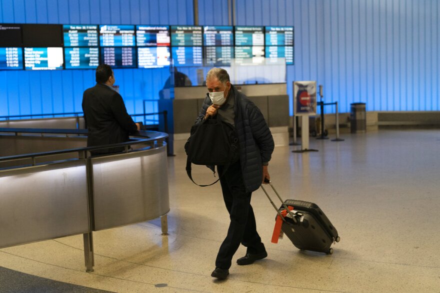 FILE - A traveler adjusts his face mask as he walks through the arrivals area at the Los Angeles International Airport in Los Angeles, Nov. 30, 2021. While all eyes are on the new and little-understood omicron variant, the delta form of the coronavirus isn't finished wreaking havoc in the U.S. (AP Photo/Jae C. Hong, File)