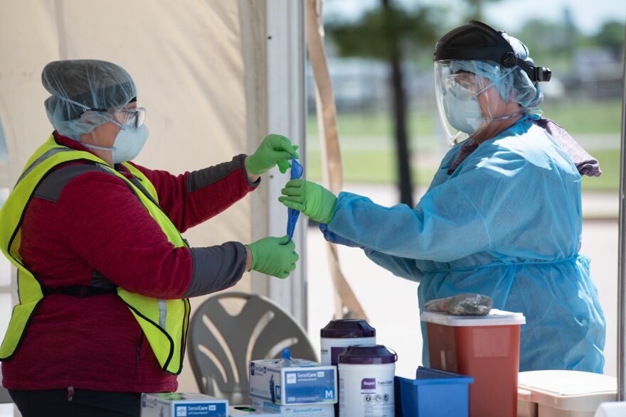 A nurse who performs nasal swabs for COVID-19 testing puts on a second layer of gloves at the Chickasaw Nation Purcell Health Cllnic.