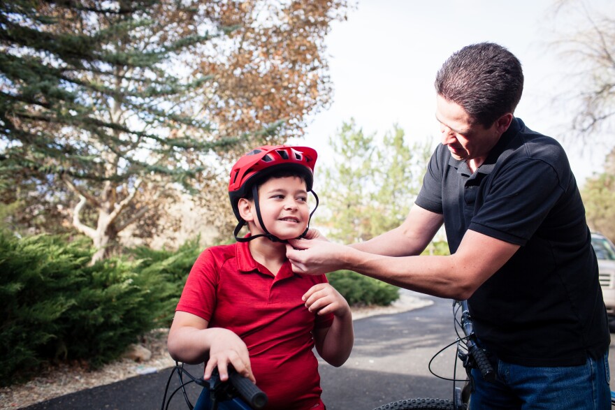 Adam Woodrum and his son, Robert, get ready for a bike ride near their home in Carson City, Nev., this month. During the summer, Robert had a bike accident that resulted in a hefty bill from the family's insurer. [Maggie Starbard for KHN]