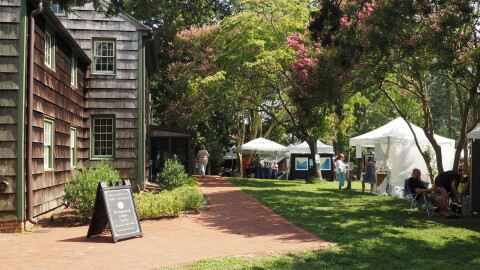 Image displaying tents of artists' work under the wooded canopy at Rehoboth Art League's wooded campus.
