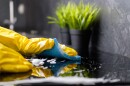 The girl washes the stove with a blue sponge in yellow gloves