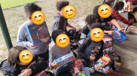 A group of children opening up various boardgames. Their faces are blurred out with smiling emojis. 