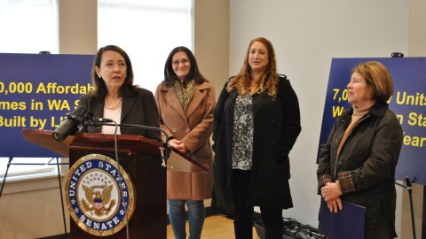 Senator Maria Cantwell stands at a brown podium alongside Spokane Mayor Lisa Brown, while two other affordable housing advocates in winter jackets stand behind them.