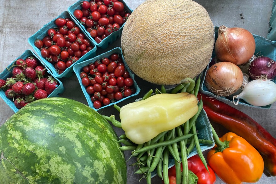 Strawberries, melons, tomatoes, onions, peppers and green beans lay on a table.