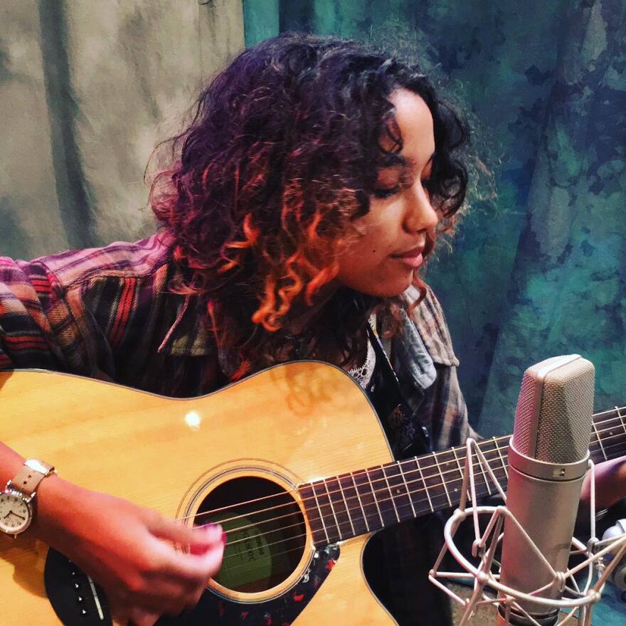 A woman in a radio studio playing a guitar.