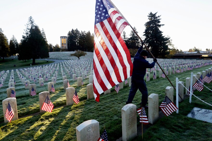 A larger American flag is raised among flag-covered graves on Veterans Day in the veterans' section of Evergreen-Washelli cemetery, on Nov. 11, 2014, in Seattle.