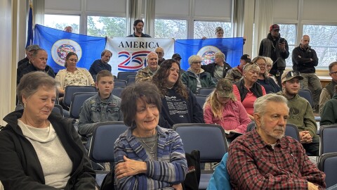 Three attendees hold two former Minnesota state flags and an "America 250" flag May 5, 2026, in the back of the Itasca County Boardroom in Grand Rapids.