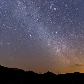 Night sky filled with stars and meteors with silhouetted hilltops