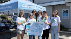 photo shows six women standing in front of a Save Our Shores tent in a parking lot. They're holding a sign that reads, "Thank you coastal cleanup volunteers."