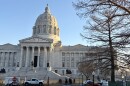 A photo of the exterior of the Missouri State capitol building. Vehicles are parked in front of the domed structure, people walk on the sidewalk. 