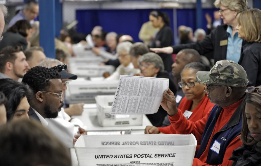 People sit at long tables picking up ballots and reading them.