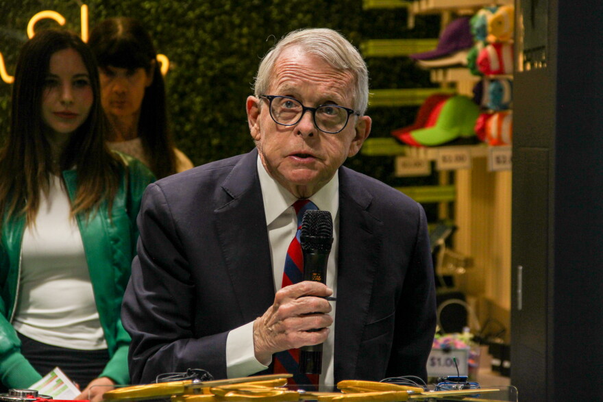 An older man with glasses speaks into a handheld microphone. 