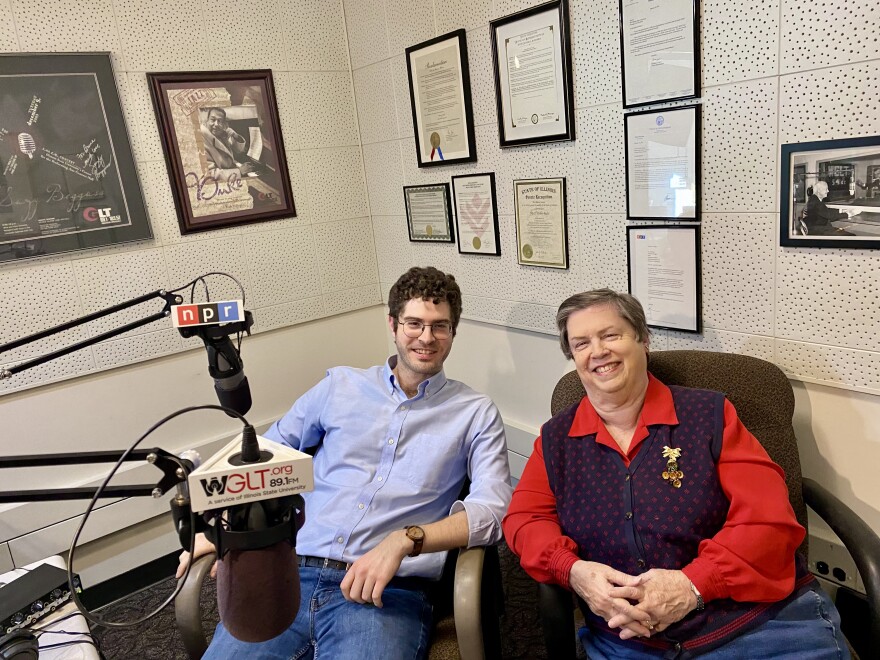 Two people sit in a radio station, smiling at the camera