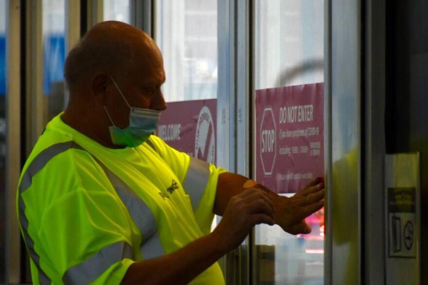 A worker at a Pilot Travel Center gas station in Greenfield, Indiana puts a sticker on the door telling patrons not to enter if they feel symptoms associated with COVID-19.