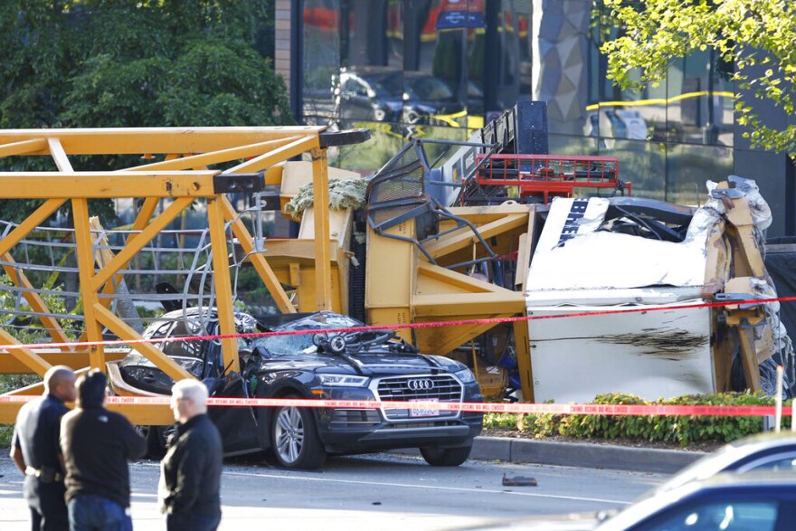 A large yellow crane resting on top of a crushed black sedan. 