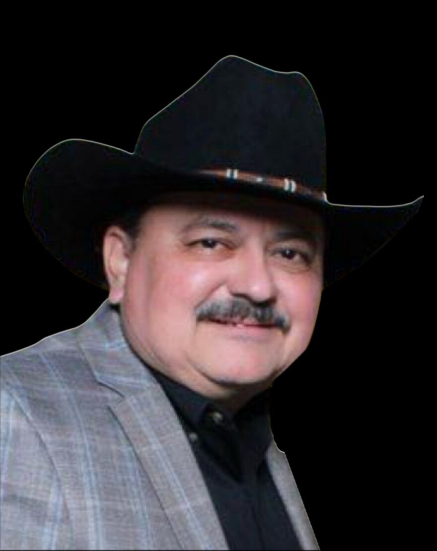 photo of a man with a mustache, who is wearing a black cowboy hat, gray and blue blazer and black shirt. 