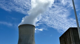 A wide shot of the Callaway Nuclear Power Plant cooling tower. It's wider at the top and bottom and white water vapor comes from the top. The sky is light blue with some slim clouds. 
