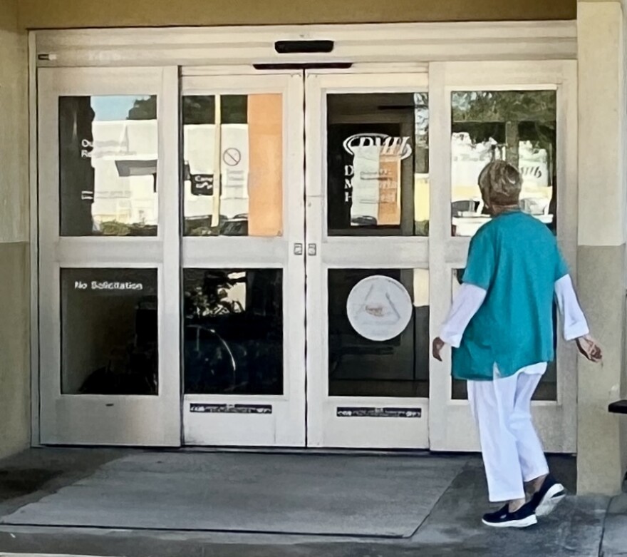 A woman in a green medical shirt and white long sleeves and pants walking into a hospital entrance