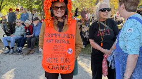 A woman wears a sign as other protesters gather behind her.