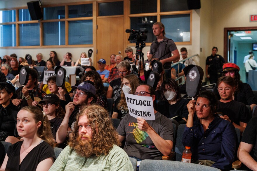 Privacy advocates hold signs meant to resemble Flock Safety cameras during a Lansing City Council meeting on Aug. 24, 2026.