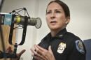 A woman wearing a Kansas City Police uniform sits inside a radio studio. She gesturing with both hands and talking at a microphone.