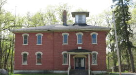 A front view of a two story red-brick building with arched windows and a wooden belfry