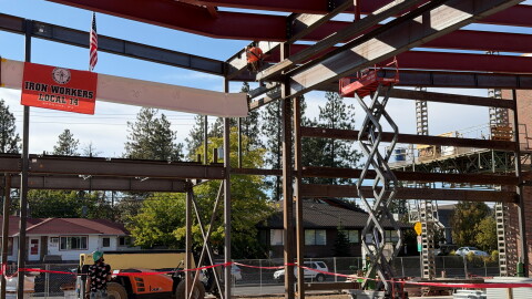 A white steel beam is lifted into place at a building under contruction.