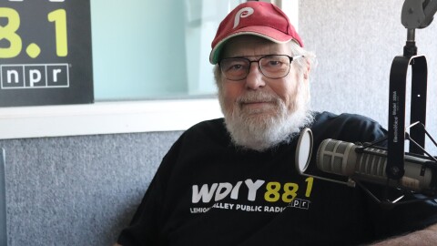 Mike McGrath sits at a table in front of microphone, wearing a black WDIY t-shirt and Philadelphia Phillies baseball hat.