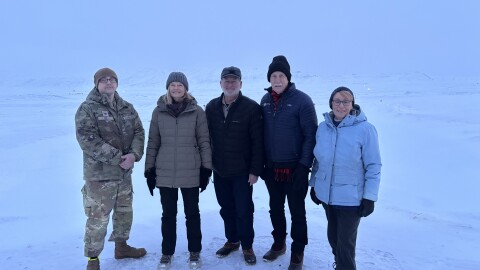 Five people in a snowy landscape, one in a military uniform