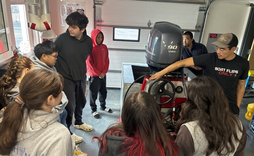 Introduction to Outboard Systems students stand around motor as course instructor Triston Chaney teaches.