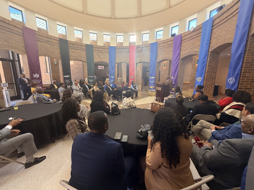 Groups of people sit around round black tables inside a rotunda.