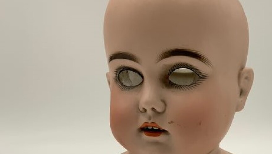 Close up of an old doll with pale skin and mirrors for eyes.